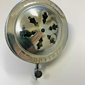 May include: A circular silver-toned metal phonograph sound box featuring a decorative star-shaped cutout pattern on the front face. The outer rim is embossed with the text His Master's Voice and SOUND BOX, with a small needle holder at the base.