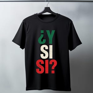 Könnte beinhalten: Ein schwarzes Kurzarm-T-Shirt mit dem Text ¿Y SI SI? in einer abgenutzten Schriftart. Die Buchstaben sind vertikal gestapelt, wobei die obere Zeile grün, die mittlere cremeweiß und die untere rot ist, mittig auf der Brust platziert.