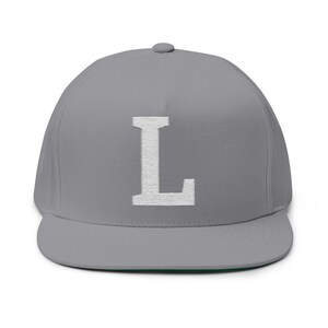 Könnte beinhalten: Graue Baseballkappe mit flachem Schirm und einem weißen, gestickten Buchstaben "L" auf der Vorderseite. Die Kappe hat eine strukturierte Krone und einen flachen Schirm. Die Unterseite des Schirms ist grün.