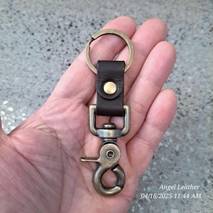 May include: A brown leather key chain with a brass key ring and a brass swivel hook. The key chain has a brass button on the leather strap.  Angel Leather 04/18/2025 11:44 AM