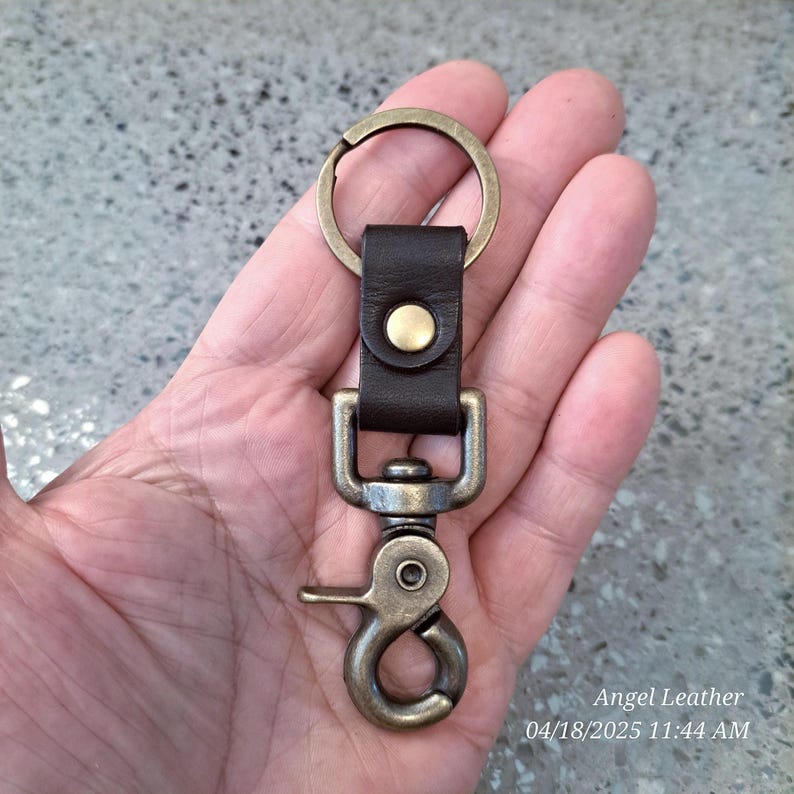 May include: A brown leather key chain with a brass key ring and a brass swivel hook. The key chain has a brass button on the leather strap.  Angel Leather 04/18/2025 11:44 AM