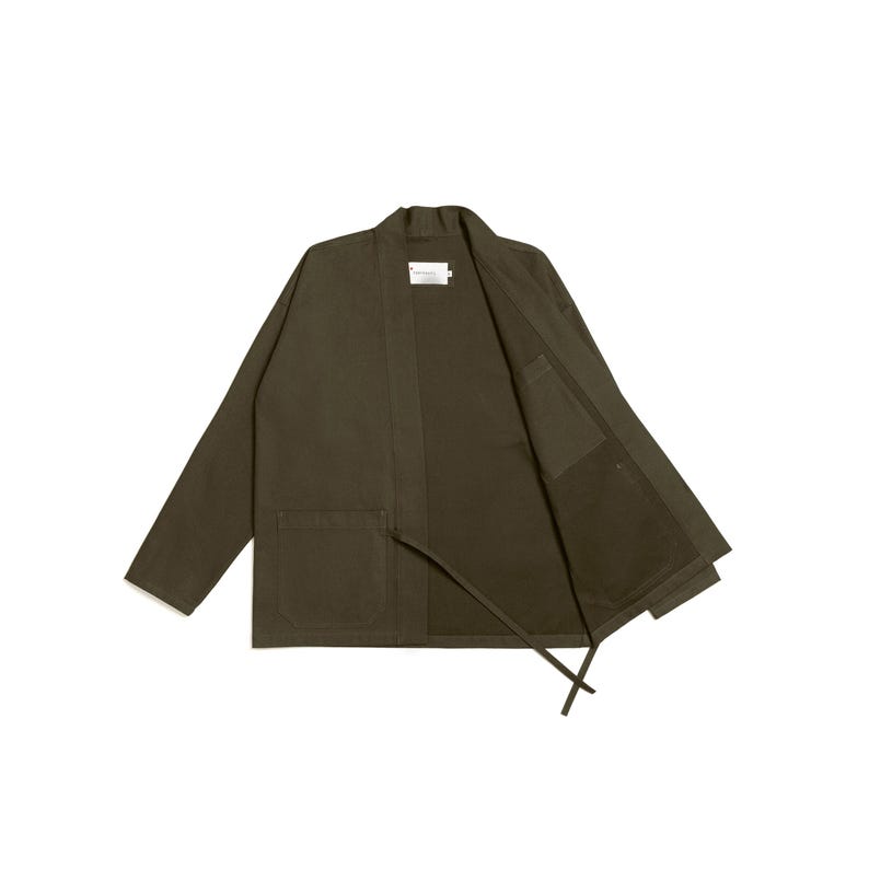 Puede incluir: Una chaqueta de color verde oliva abierta por delante con mangas largas, cuello tipo chal y dos grandes bolsillos de parche en la parte frontal. La prenda incluye una peque&ntilde;a etiqueta rectangular blanca en el cuello y dos finas cintas de tela.