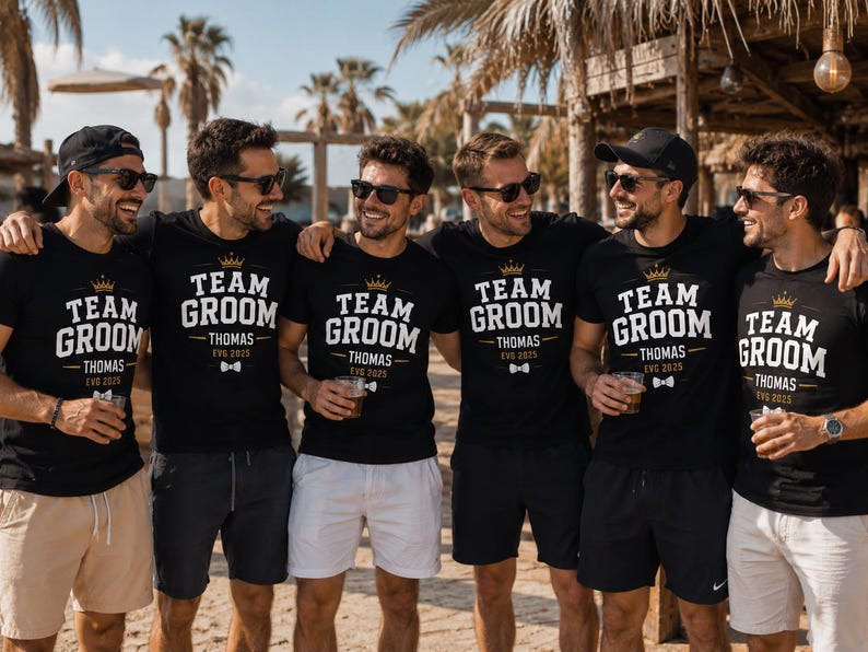 May include: Six black t-shirts featuring white text that reads TEAM GROOM, the name THOMAS, and the date EVG 2025. Each shirt includes a gold crown graphic above the text and a small white bow tie graphic below the name, worn by six individuals.
