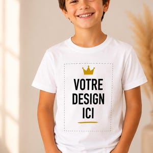 May include: A white short-sleeved t-shirt featuring a rectangular dashed border, a gold crown icon, and the black text "VOTRE DESIGN ICI" centred on the chest, paired with blue denim jeans. The design includes a small gold horizontal line.