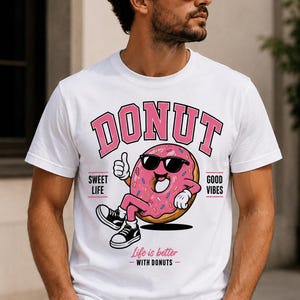 Pu&ograve; includere: Una t-shirt bianca con la grafica di una ciambella glassata rosa con zuccherini, che indossa occhiali da sole neri e scarpe da ginnastica nere. Il testo recita DONUT, SWEET LIFE, GOOD VIBES e Life is better WITH DONUTS in caratteri rosa e neri.