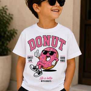 May include: A white short-sleeved t-shirt featuring a graphic of a pink donut with sunglasses, arms, and legs. The text reads DONUT, SWEET LIFE, GOOD VIBES, and Life is better WITH DONUTS. The donut character is giving a thumbs up gesture.