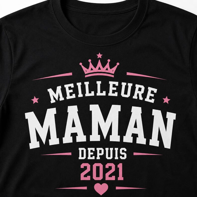 Puede incluir: Una camiseta negra con un dise&ntilde;o gr&aacute;fico que presenta una corona rosa en la parte superior, el texto blanco MEILLEURE MAMAN y el texto rosa DEPUIS 2021 debajo. El dise&ntilde;o incluye estrellas rosas a los lados y un peque&ntilde;o coraz&oacute;n rosa en el centro.
