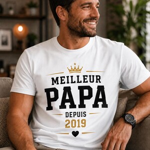 May include: A white short-sleeved t-shirt featuring the text MEILLEUR PAPA DEPUIS 2019 in black and gold lettering. The design includes a gold crown icon above the text, a small black heart icon below the year, and horizontal gold lines.