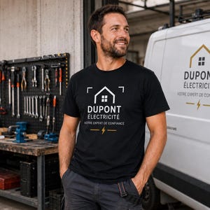 May include: A black short-sleeved t-shirt featuring a white graphic of a house outline above the text DUPONT &Eacute;LECTRICIT&Eacute; and the phrase VOTRE EXPERT DE CONFIANCE with a small yellow lightning bolt icon centered below the text.