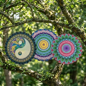 May include: Three colorful, round mandala ornaments hanging from a tree branch. The ornaments feature intricate designs in shades of blue, green, purple, pink, and yellow. One has a yin-yang symbol, another a floral pattern, and the third a vibrant mandala.