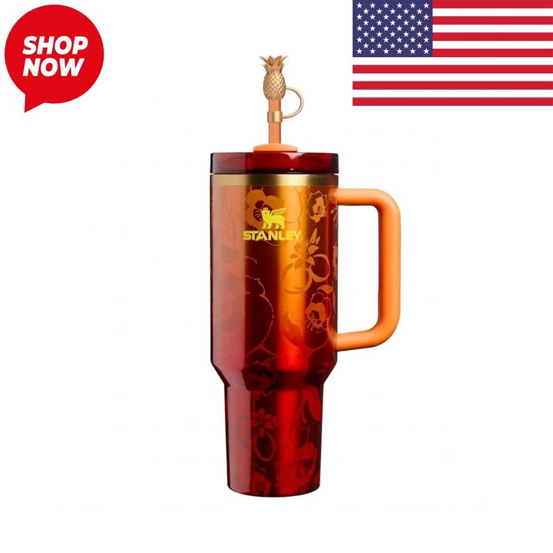 May include: A tall, cylindrical Stanley tumbler in a deep red gradient finish with a floral pattern. It features a gold-toned rim, a sturdy orange side handle, and a lid topped with a small, metallic gold pineapple-shaped decorative topper.