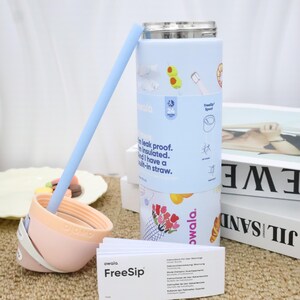 May include: A light blue Owala FreeSip insulated water bottle with a built-in straw. The bottle has a stainless steel lid and is decorated with colorful food illustrations. Includes a light blue straw and a pink and white lid.