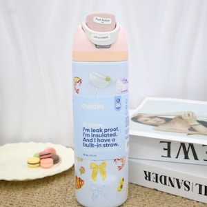 May include: A pastel-colored Owala water bottle with a push-button lid. The bottle features a light blue section with food-themed stickers and text that reads, "Hi there. I'm leak proof. I'm insulated. And I have a built-in straw." It holds 34 oz.