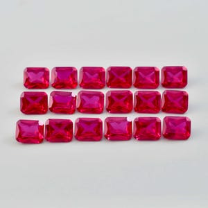 Puede incluir: Dieciocho piedras preciosas de color rosa intenso, con corte rectangular, dispuestas en tres filas ordenadas de seis. Cada piedra presenta una superficie facetada que refleja la luz, creando un aspecto brillante y centelleante en el color.