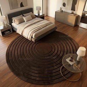 May include: A large, circular, dark brown area rug featuring a concentric ring pattern with deep, recessed grooves. The rug is positioned on a wooden floor in a bedroom setting, with the text FZRUGSART visible in multiple locations on the surface.