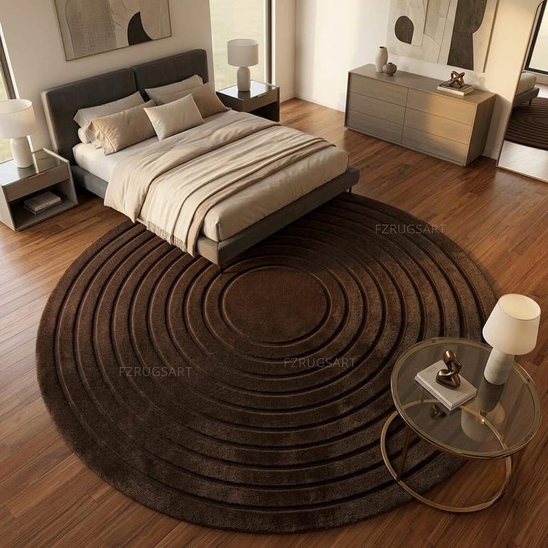 May include: A large, circular, dark brown area rug featuring a concentric ring pattern with deep, recessed grooves. The rug is positioned on a wooden floor in a bedroom setting, with the text FZRUGSART visible in multiple locations on the surface.
