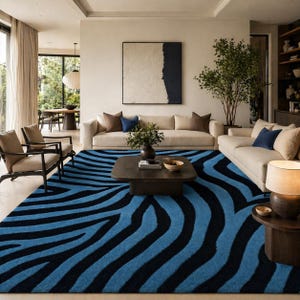 May include: A large rectangular area rug featuring a bold, repeating zebra stripe pattern in vibrant blue and deep black. The rug covers the floor space in a living room, extending from the foreground toward the beige sofas and wooden coffee table.