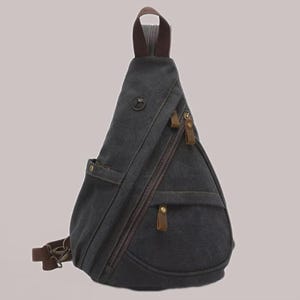 May include: Dark gray canvas sling bag with brown leather accents. Features a zippered main compartment, a front pocket, and an adjustable shoulder strap. The bag has a top handle and a small logo on the front. A stylish and practical accessory.