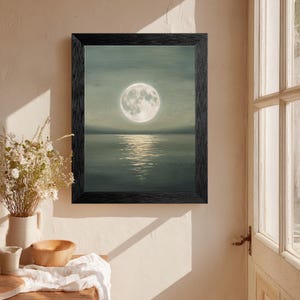 May include: A framed wall art print featuring a full moon centered above a calm body of water. The painting uses muted sage green and gray tones to depict a night sky and a reflective moonlit surface, enclosed in a textured black wooden frame.