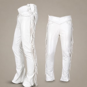 Puede incluir: Un pantalón blanco con largos flecos a lo largo de las costuras exteriores, un diseño de cintura alta con tres botones en el lateral y costuras decorativas a lo largo de los bolsillos y el dobladillo, mostrado de perfil y de frente.