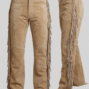 May include: Tan suede leather pants featuring long fringe detailing along the outer seams of both legs. The pants include a standard waistband with a button closure, front pockets, and a straight-leg cut, shown from both front and side angles.
