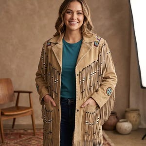 Puede incluir: Una chaqueta de ante color tostado con largos flecos en el pecho, las mangas y el dobladillo. La chaqueta incluye cuentas decorativas en los flecos, bordados geométricos coloridos en los hombros y parches circulares con cuentas en las mangas.