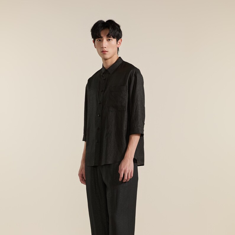 Puede incluir: Una camisa negra de botones con mangas tres cuartos y un bolsillo en el pecho, combinada con pantalones negros a juego. La camisa presenta un cuello est&aacute;ndar y una tapeta de botones frontal, confeccionada en un tejido texturizado.