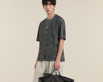 Camiseta gris de corte relajado para hombre, mezcla de algodón con estampado floral en tonos neutros, prenda minimalista de verano.