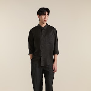 Puede incluir: Una camisa de botones de color gris carb&oacute;n oscuro con mangas de tres cuartos y un bolsillo en el pecho. La camisa presenta un cuello cl&aacute;sico, una tapeta de botones frontal y un dobladillo recto, combinada con pantalones a juego.
