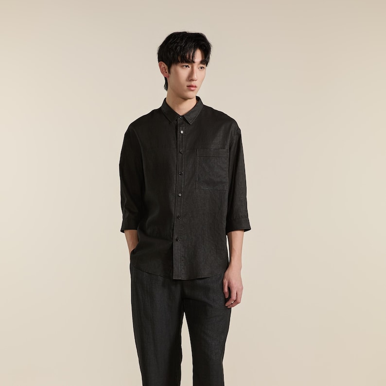 Puede incluir: Una camisa de botones de color gris carb&oacute;n oscuro con mangas de tres cuartos y un bolsillo en el pecho. La camisa presenta un cuello cl&aacute;sico, una tapeta de botones frontal y un dobladillo recto, combinada con pantalones a juego.