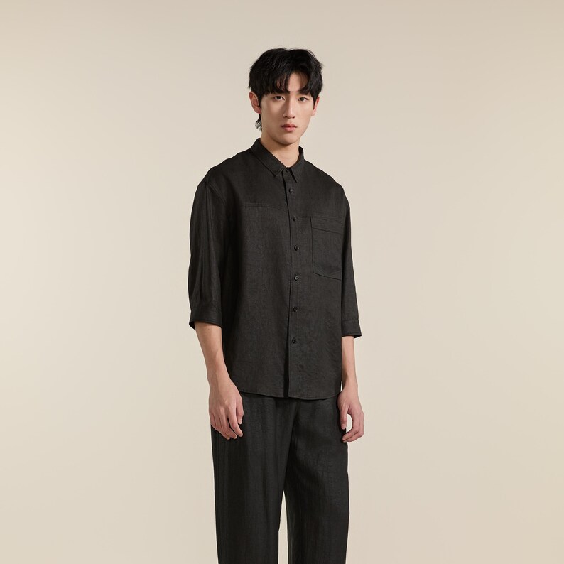 Puede incluir: Una camisa de botones gris carb&oacute;n oscuro con mangas tres cuartos, cuello cl&aacute;sico y un bolsillo en el pecho en el lado izquierdo. La camisa se combina con pantalones a juego de color gris carb&oacute;n oscuro, creando un conjunto coordinado.