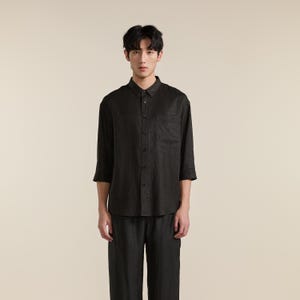 Puede incluir: Una camisa de botones gris carb&oacute;n oscuro con mangas de tres cuartos, cuello est&aacute;ndar y un bolsillo en el pecho. La camisa se combina con pantalones a juego de color gris carb&oacute;n oscuro, creando un conjunto coordinado de tela texturizada.