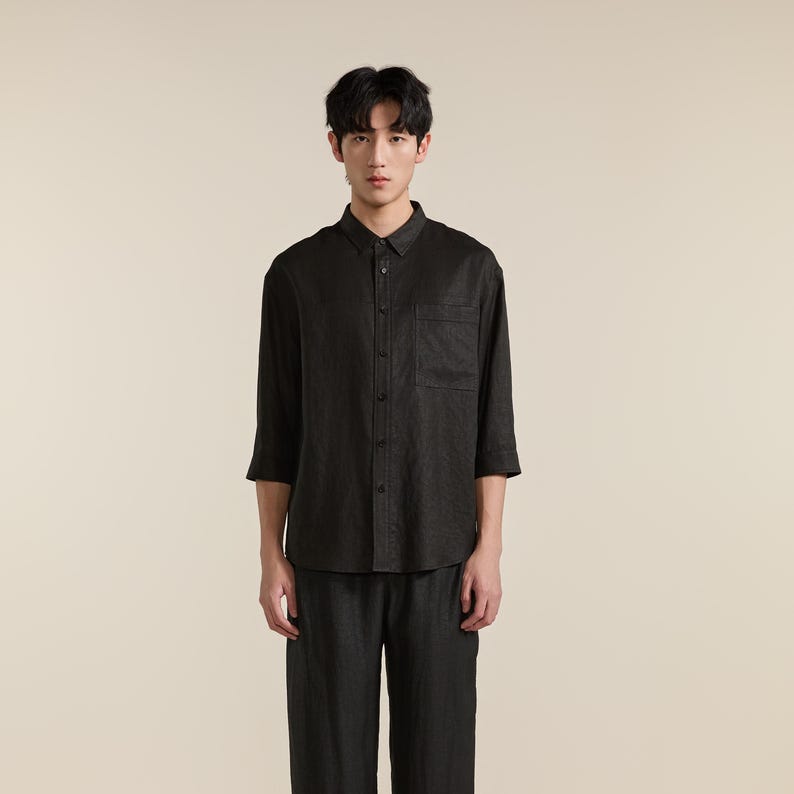 Puede incluir: Una camisa de botones gris carb&oacute;n oscuro con mangas de tres cuartos, cuello est&aacute;ndar y un bolsillo en el pecho. La camisa se combina con pantalones a juego de color gris carb&oacute;n oscuro, creando un conjunto coordinado de tela texturizada.