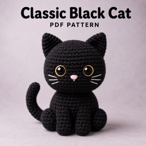 May include: A black crocheted cat toy with large glossy eyes, a small pink nose, and white embroidered whiskers. The text above the cat reads Classic Black Cat PDF PATTERN. The cat has pointed ears and a curved tail, sitting in a seated position.