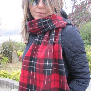 May include: A red and black plaid scarf with white accents. The scarf is made of a soft, fuzzy material and is worn around the neck of a person.
