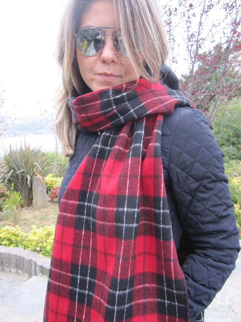 May include: A red and black plaid scarf with white accents. The scarf is made of a soft, fuzzy material and is worn around the neck of a person.