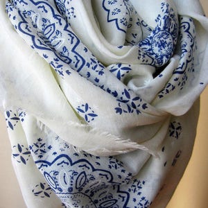 May include: White scarf with a blue paisley pattern. The scarf is made of a soft, lightweight fabric and is perfect for adding a touch of style to any outfit.
