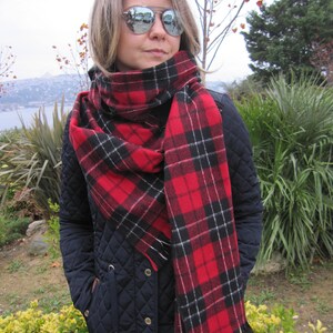May include: A red and black plaid scarf with white accents. The scarf is wrapped around the neck of a person wearing a black quilted jacket.