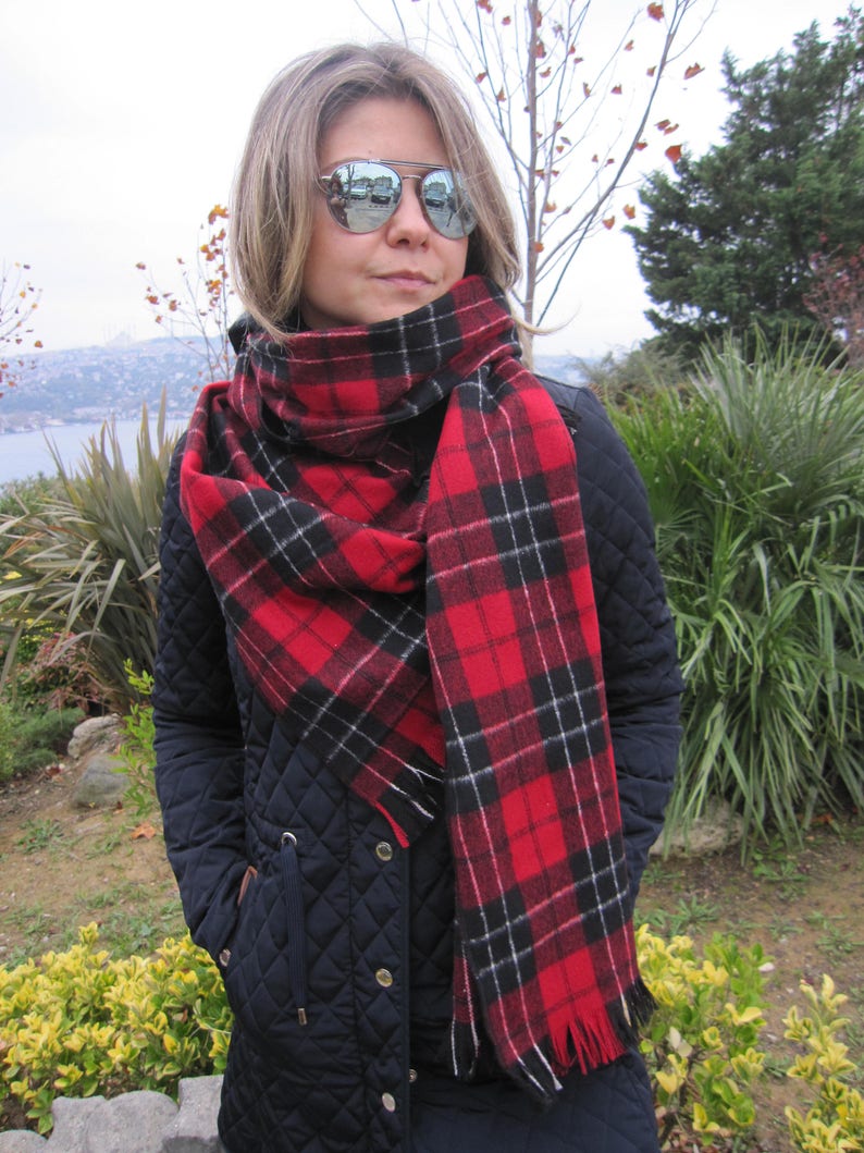 May include: A red and black plaid scarf with white accents. The scarf is wrapped around the neck of a person wearing a black quilted jacket.
