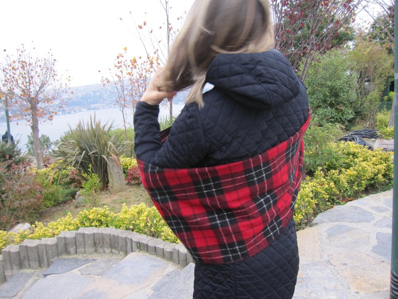 May include: A black quilted jacket with a red and black plaid scarf. The scarf is wrapped around the neck and shoulders.