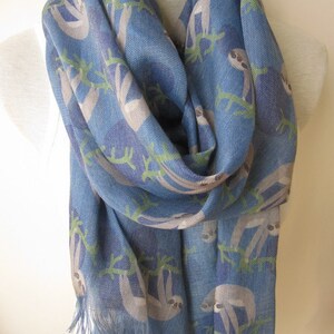May include: A blue scarf with a pattern of sloths hanging from branches. The scarf has a fringe on the bottom.