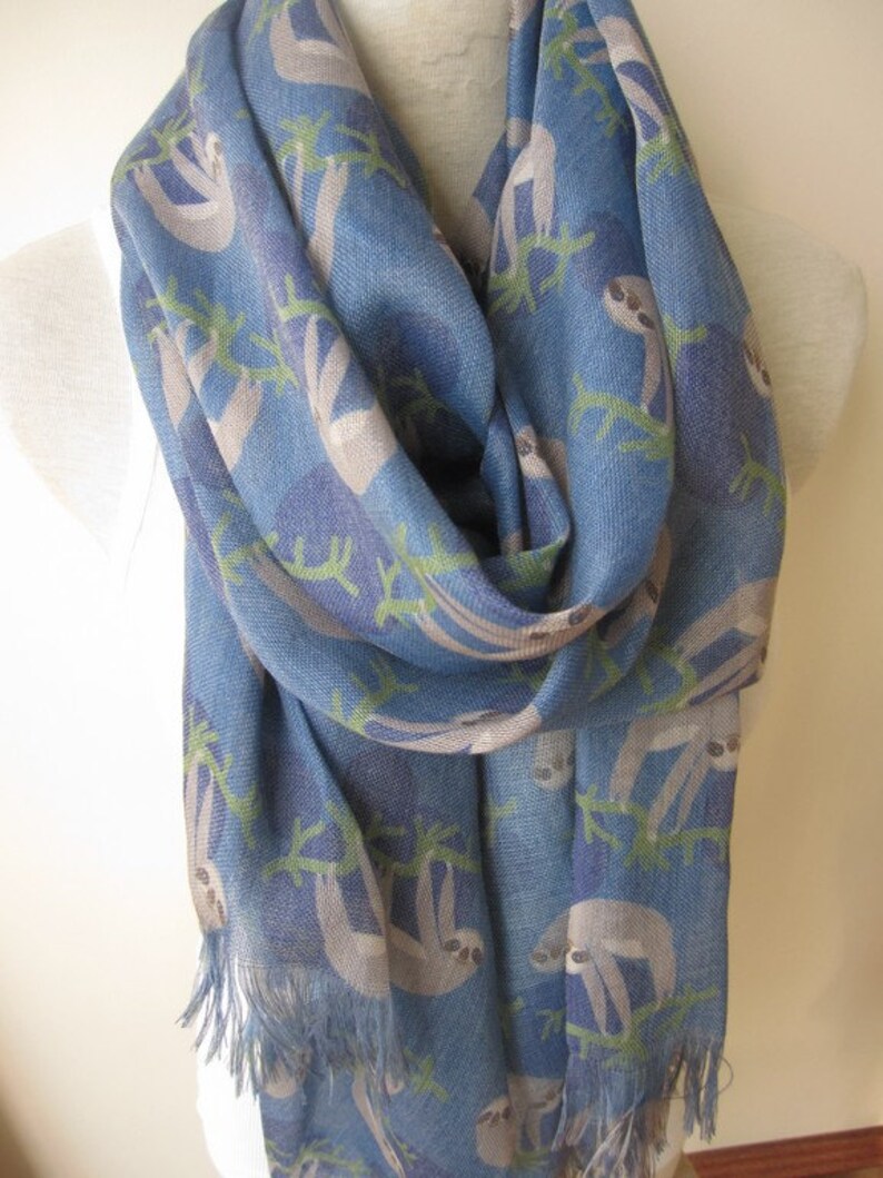 May include: A blue scarf with a pattern of sloths hanging from branches. The scarf has a fringe on the bottom.