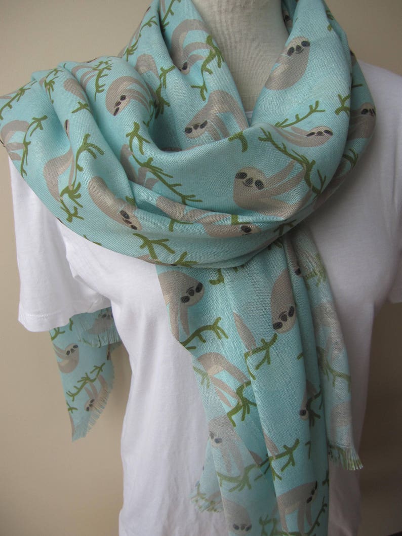 May include: A light blue scarf with a pattern of sloths hanging from branches. The sloths are a light brown color with black eyes.