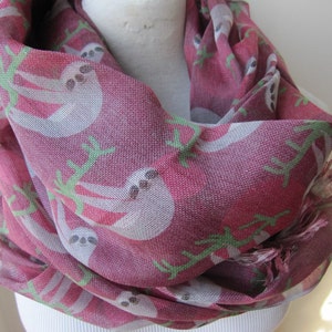 May include: A burgundy scarf with a white sloth pattern and green leaves. The scarf is made of a soft, lightweight fabric.