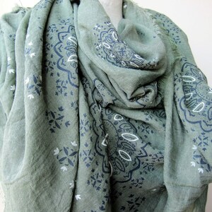May include: A green scarf with a black and white paisley pattern. The scarf is made of a soft, lightweight fabric and has a fringed edge.