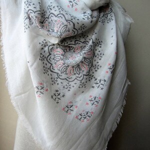 May include: White cotton scarf with a gray and pink paisley pattern. The scarf has a fringed edge.