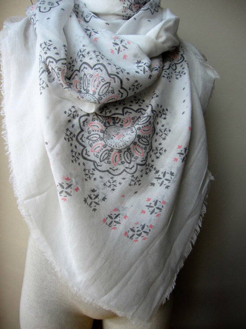 May include: White cotton scarf with a gray and pink paisley pattern. The scarf has a fringed edge.