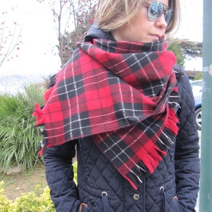 May include: A woman wearing a black quilted jacket with a red and black plaid scarf. The scarf is tied around her neck and the ends are hanging down.