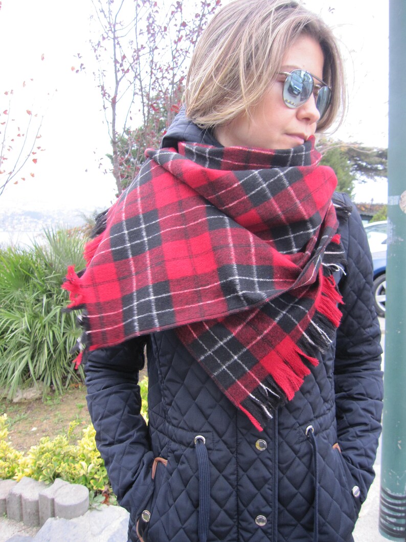 May include: A woman wearing a black quilted jacket with a red and black plaid scarf. The scarf is tied around her neck and the ends are hanging down.