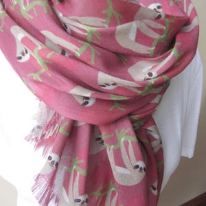 May include: A pink scarf with a pattern of sloths hanging from branches. The scarf has a fringed edge.